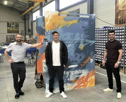 De gauche à droite : Olivier Cuenot, responsable industriel, Benjamin Locatelli, graffeur et Antoine Marceau, chargé d’affaires, devant la machine anniversaire taguée.